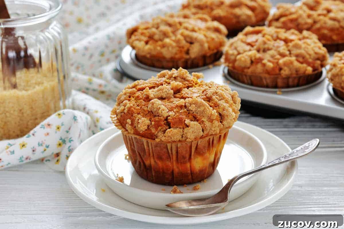 33 Irresistible Fall Desserts That Defy Portion Control 2 A crumb-topped muffin sits on a white plate with a spoon; more muffins are in a baking tray in the background, next to a jar of brown sugar.