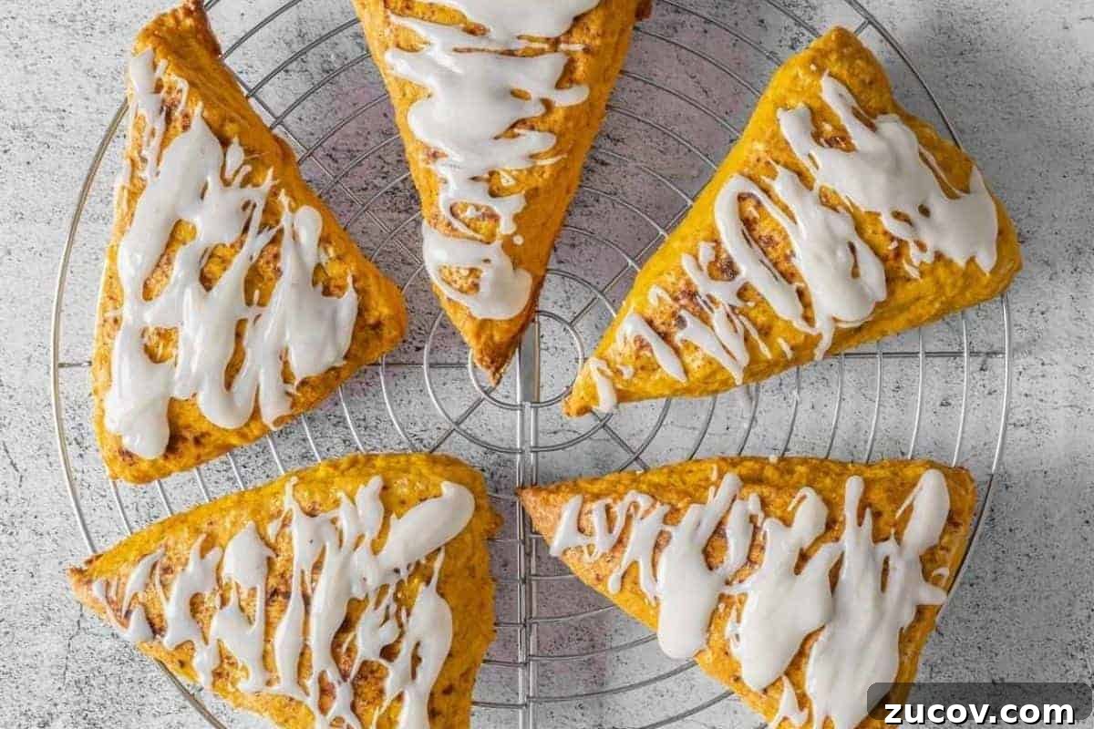 33 Irresistible Fall Desserts That Defy Portion Control 17 Five Pumpkin Spice scones with vanilla glaze are arranged in a circle on a round metal cooling rack over a light-colored surface.