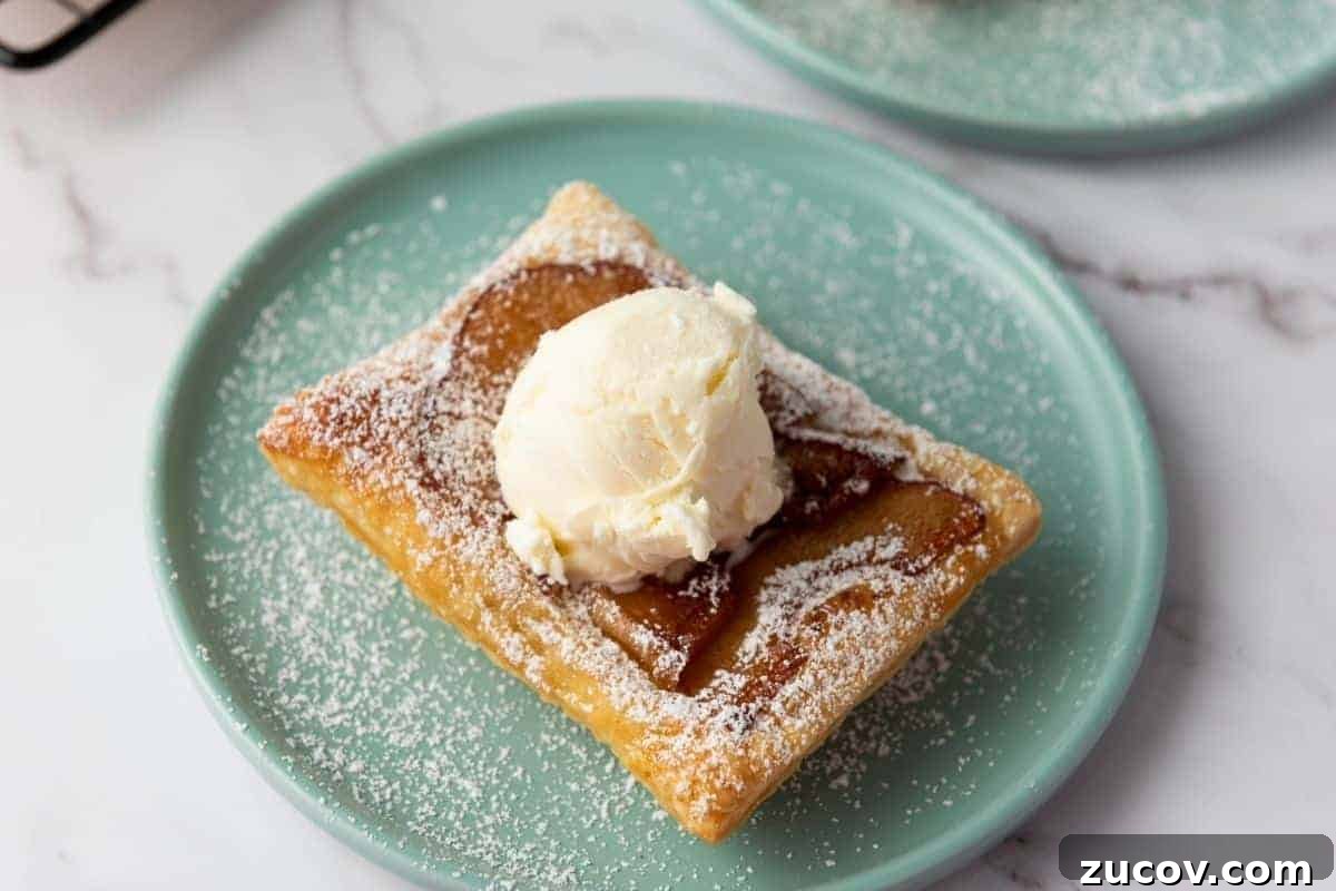 33 Irresistible Fall Desserts That Defy Portion Control 3 A Puff Pastry Apple Tart topped with a scoop of vanilla ice cream and sprinkled with powdered sugar sits on a light green plate.