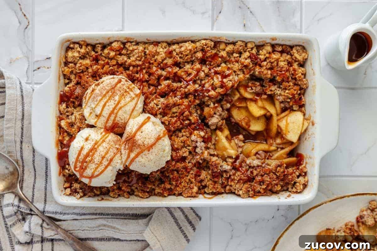 33 Irresistible Fall Desserts That Defy Portion Control 21 An Apple Crisp with Vanilla Ice Cream, served in a rectangular dish, topped with two scoops of vanilla ice cream and a caramel drizzle, accompanied by a portion on a plate beside it.