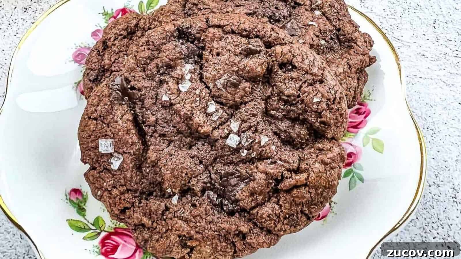 33 Irresistible Fall Desserts That Defy Portion Control 23 A close-up of a large chocolate cookie sprinkled with coarse salt, placed on a decorative plate with pink rose patterns.