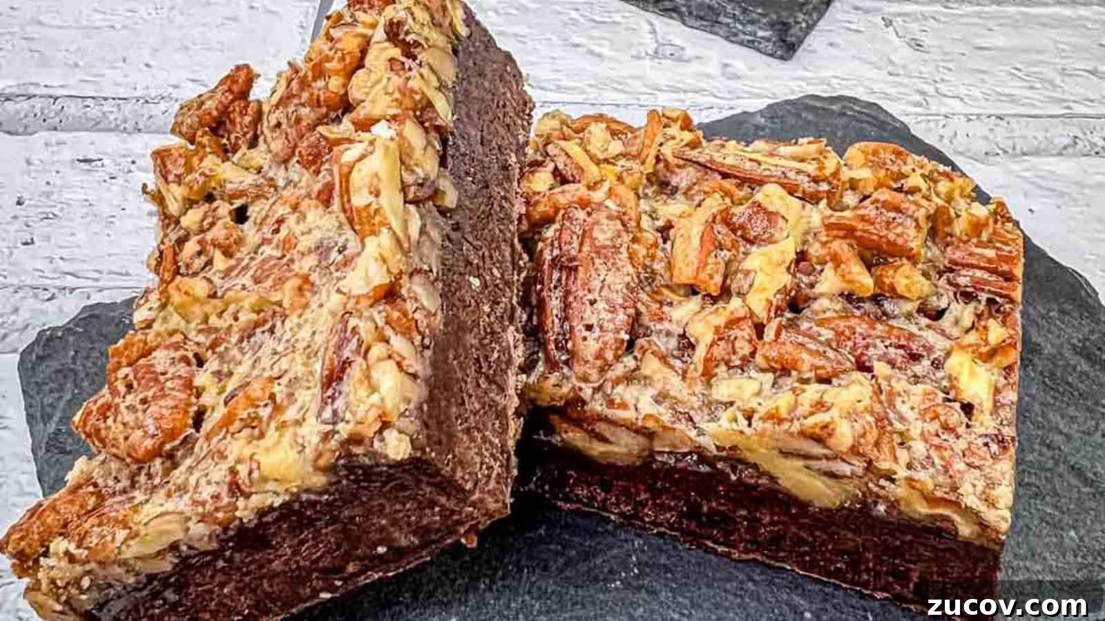 33 Irresistible Fall Desserts That Defy Portion Control 25 A close-up of two pecan brownies on a slate surface, showing the rich, chocolatey interior and a topping of chopped pecans.