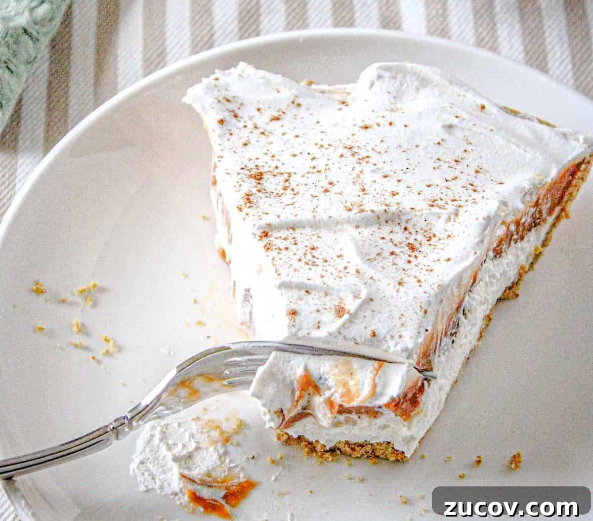 33 Irresistible Fall Desserts That Defy Portion Control 30 A slice of no-bake pumpkin cheesecake delight on a white plate, partially eaten with a fork resting on the plate.