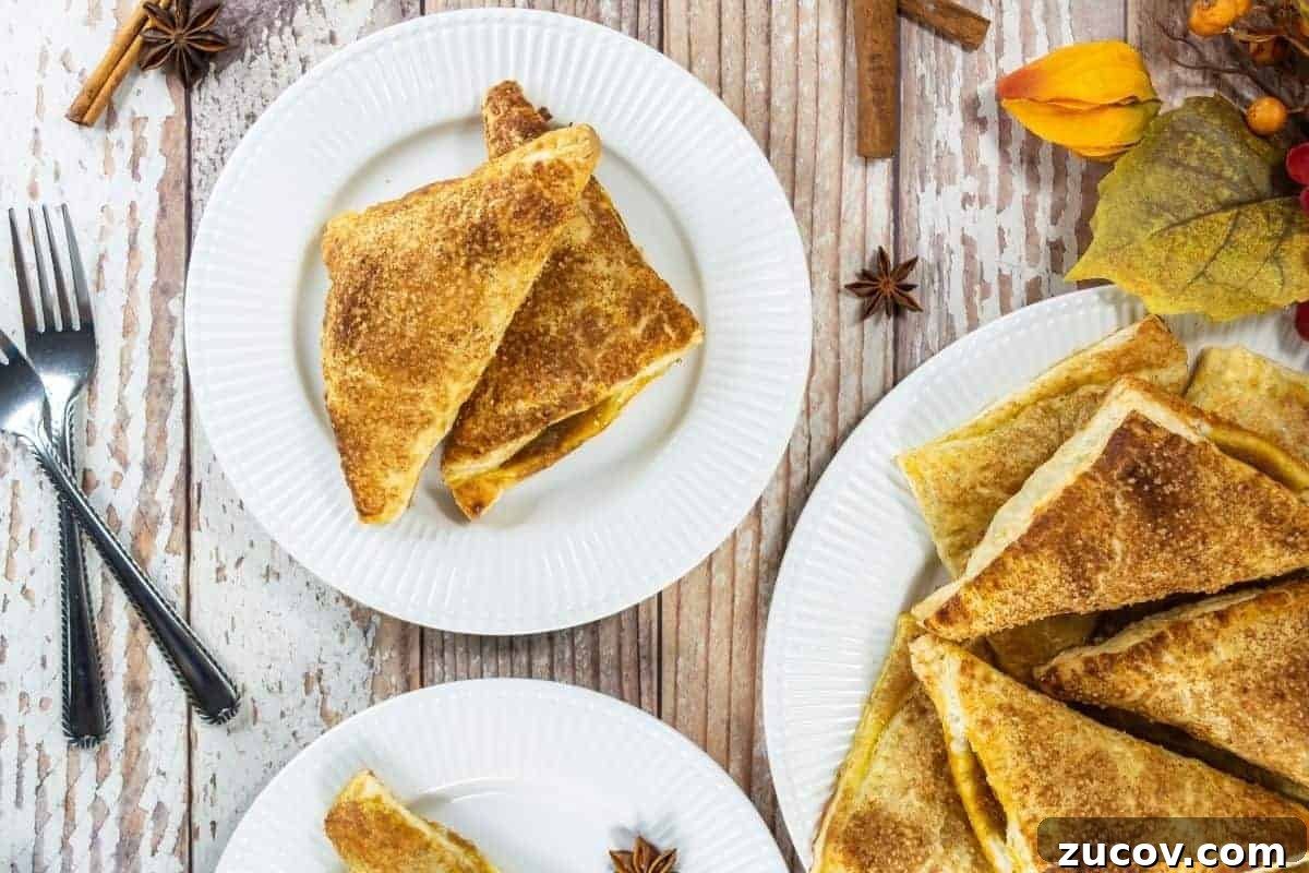 33 Irresistible Fall Desserts That Defy Portion Control 7 Three white plates with pumpkin turnovers topped with cinnamon sugar, on a rustic wooden table with utensils and autumn-themed decorations.