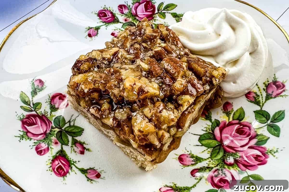 33 Irresistible Fall Desserts That Defy Portion Control 9 A slice of maple pecan pie bar topped with chopped pecans sits on a floral-patterned plate.