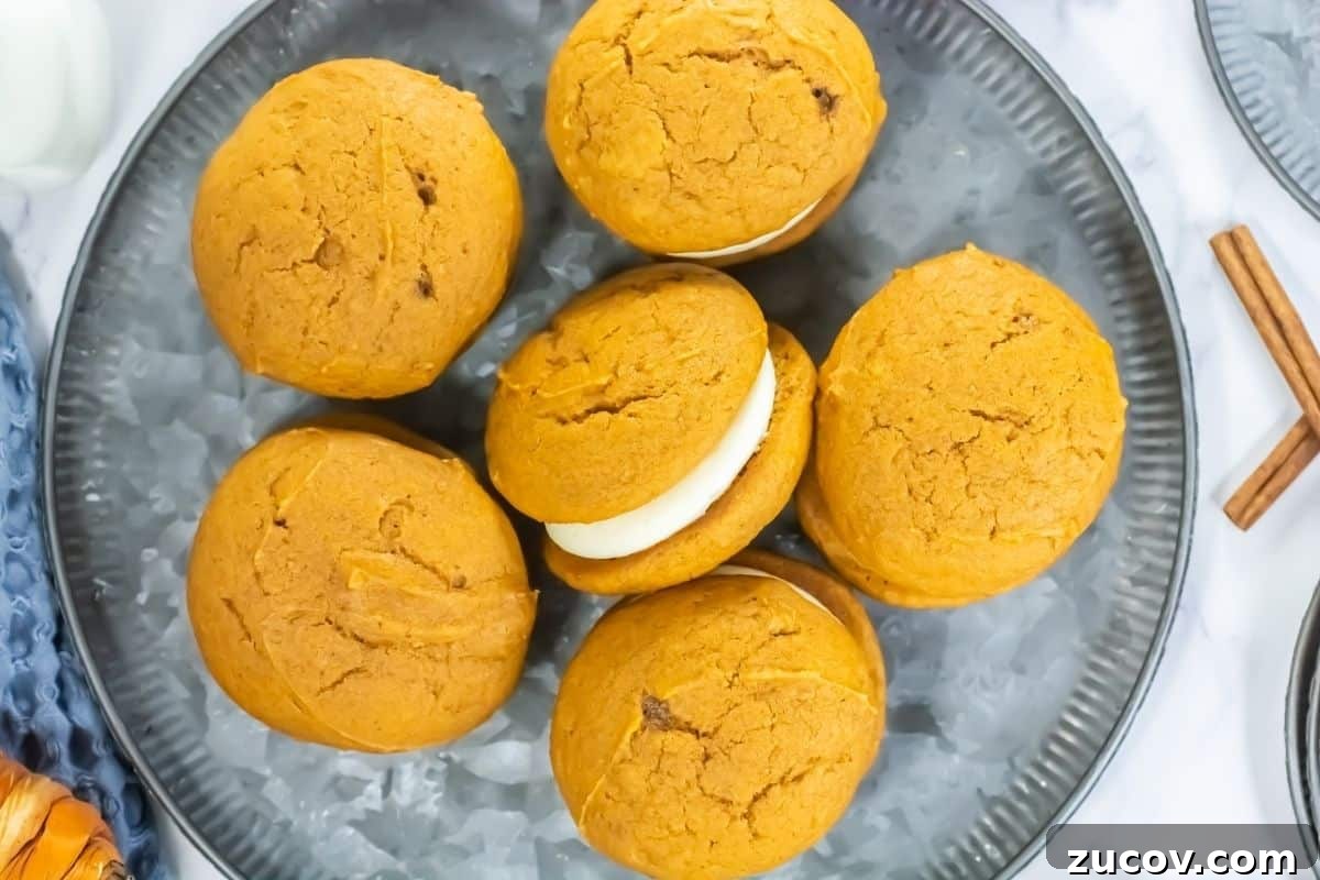 33 Irresistible Fall Desserts That Defy Portion Control 10 Six pumpkin whoopie pies with cream filling are arranged on a gray plate, viewed from above. Two cinnamon sticks are visible at the edge of the plate.