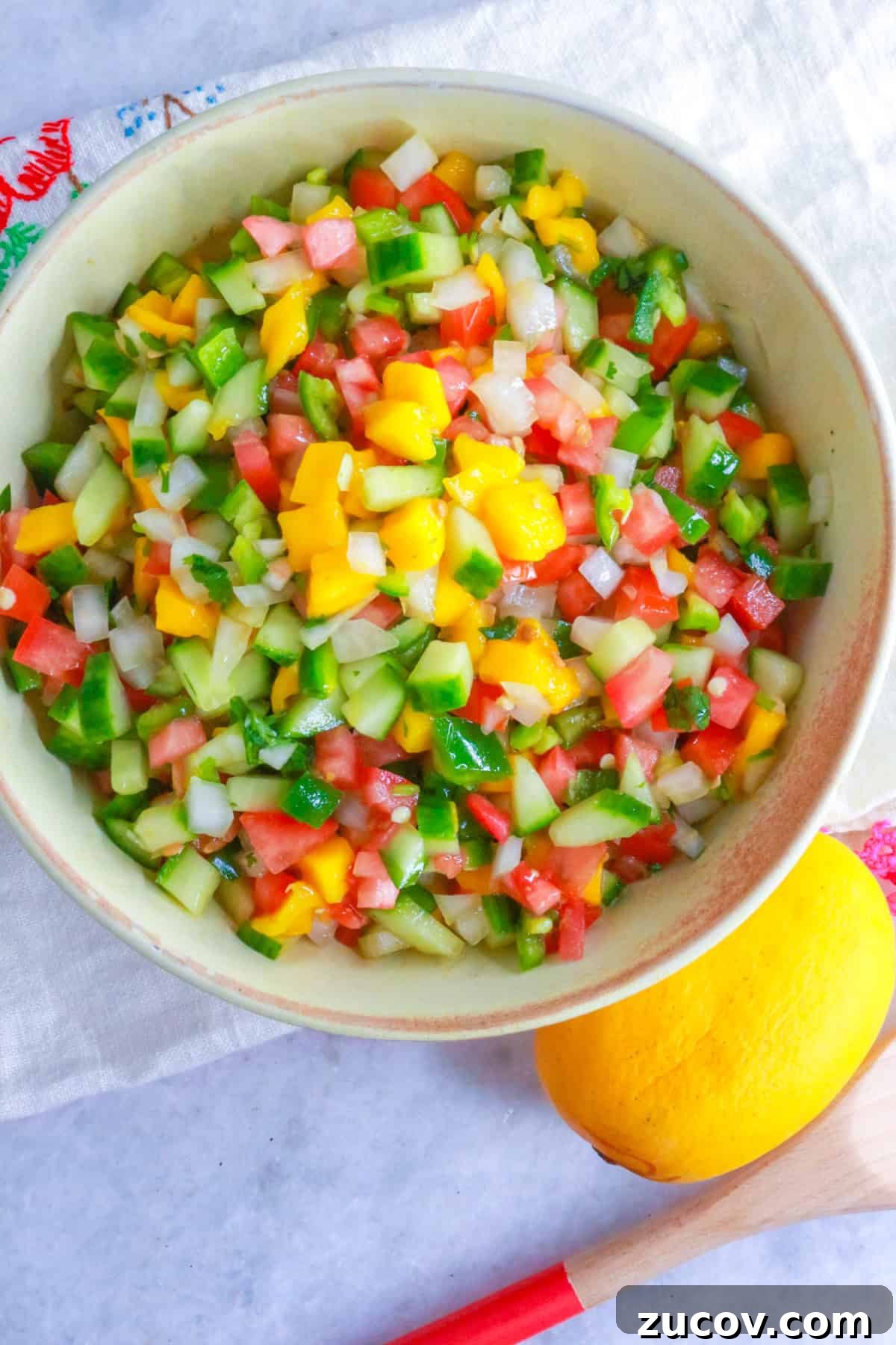 Mango pico de gallo in a bowl with a mango and wooden spoon by it