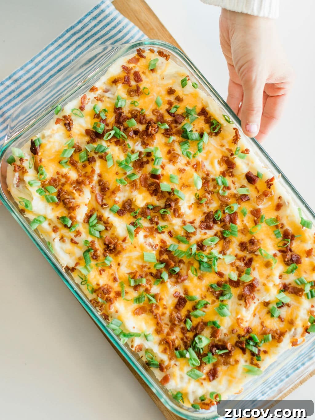 Creamy Loaded Mashed Potato Casserole with Bacon and Cheddar 2 Casserole out of the oven set on a wood cutting board and striped towel