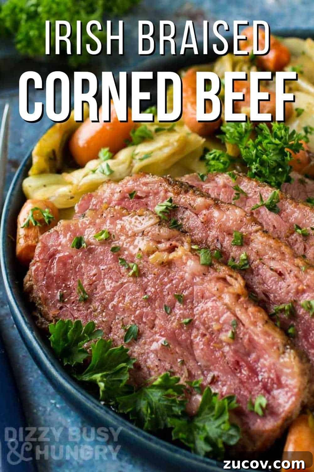 Irish Braised Corned Beef with Cabbage Recipe for St. Patrick’s Day 2 Side close up view of braised corned beef with vegetables garnished with herbs on a black plate with forks and herbs on the side on a blue cloth.