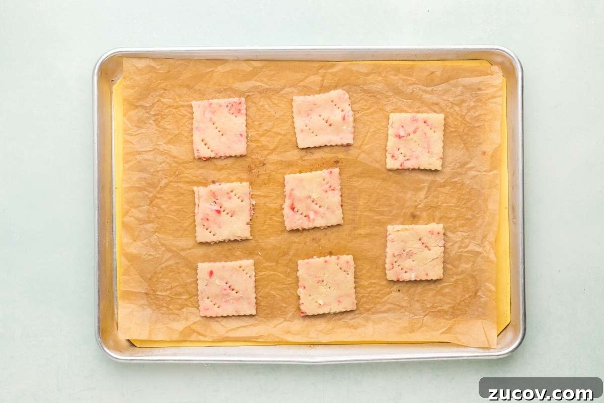 Peppermint Shortbread Cookies with White Chocolate Drizzle Recipe 8 Unbaked peppermint shortbread squares on a parchment-lined baking sheet.