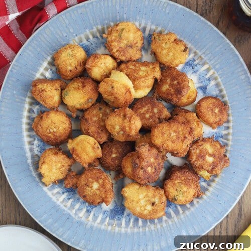 blue platter of squash puppies with a red and white checked napkin, iced tea, bowl of sauce and serving plate with one squash puppy to the side