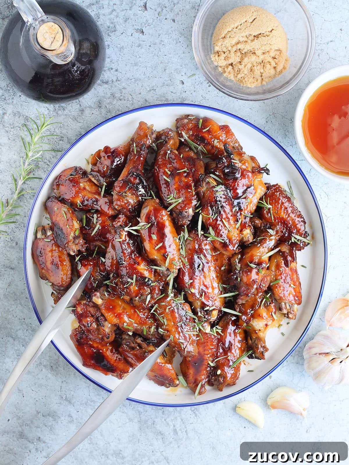 Sticky Honey Garlic Chicken Wings Recipe for Crispy Oven-Baked Wings 14 Large plate of honey garlic chicken wings garnished with fresh rosemary leaves.