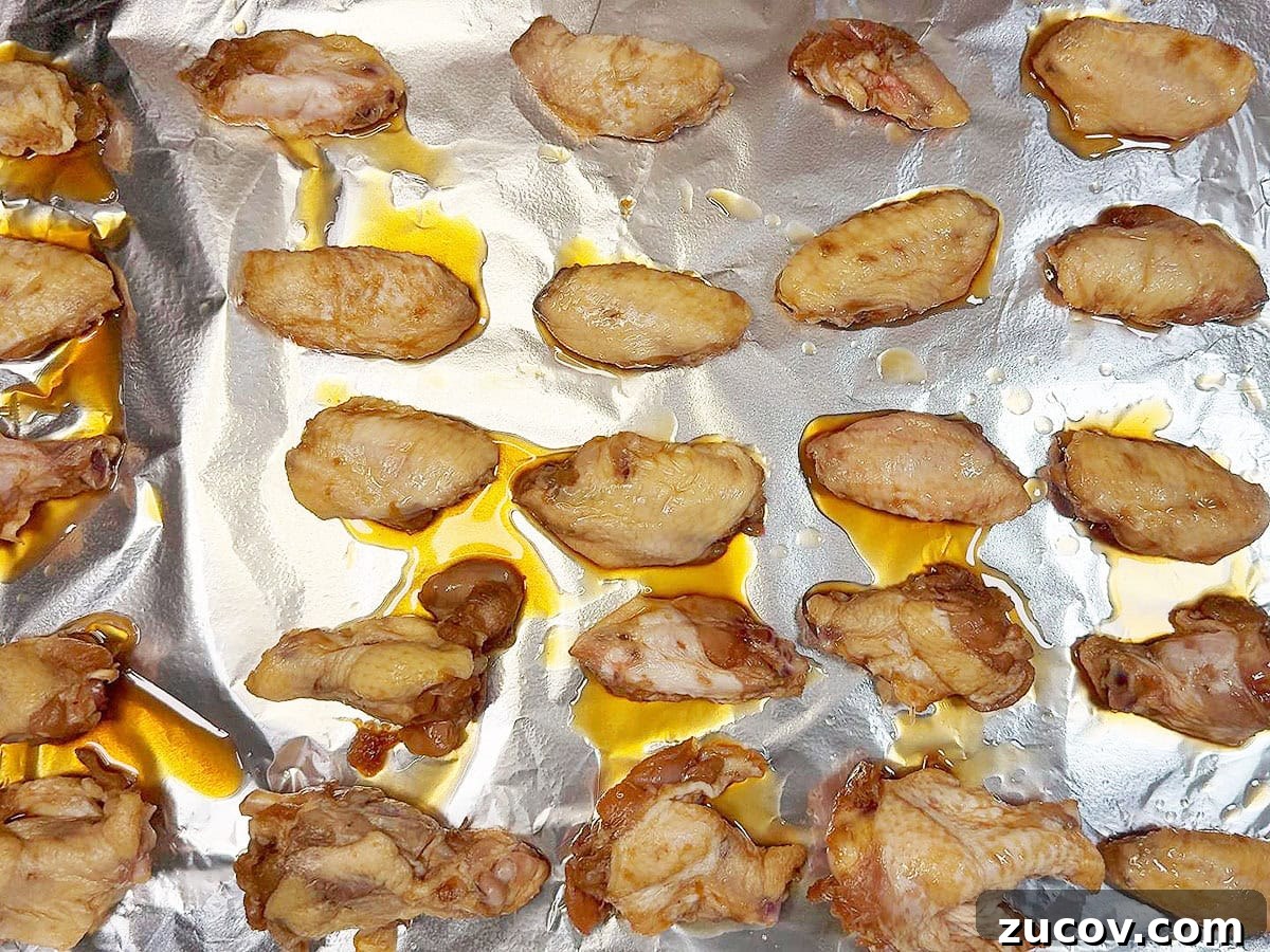 Sticky Honey Garlic Chicken Wings Recipe for Crispy Oven-Baked Wings 6 Marinated unbaked chicken wings on a foiled lined baking sheet.