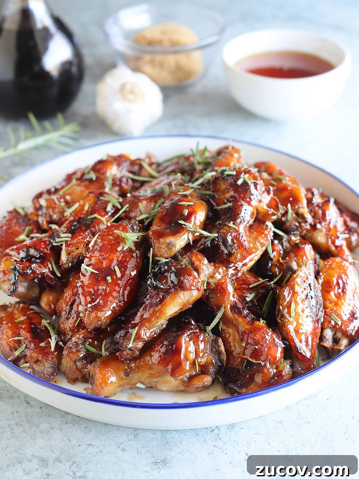 Sticky Honey Garlic Chicken Wings Recipe for Crispy Oven-Baked Wings 9 Large plate of honey garlic chicken wings garnished with fresh rosemary leaves.