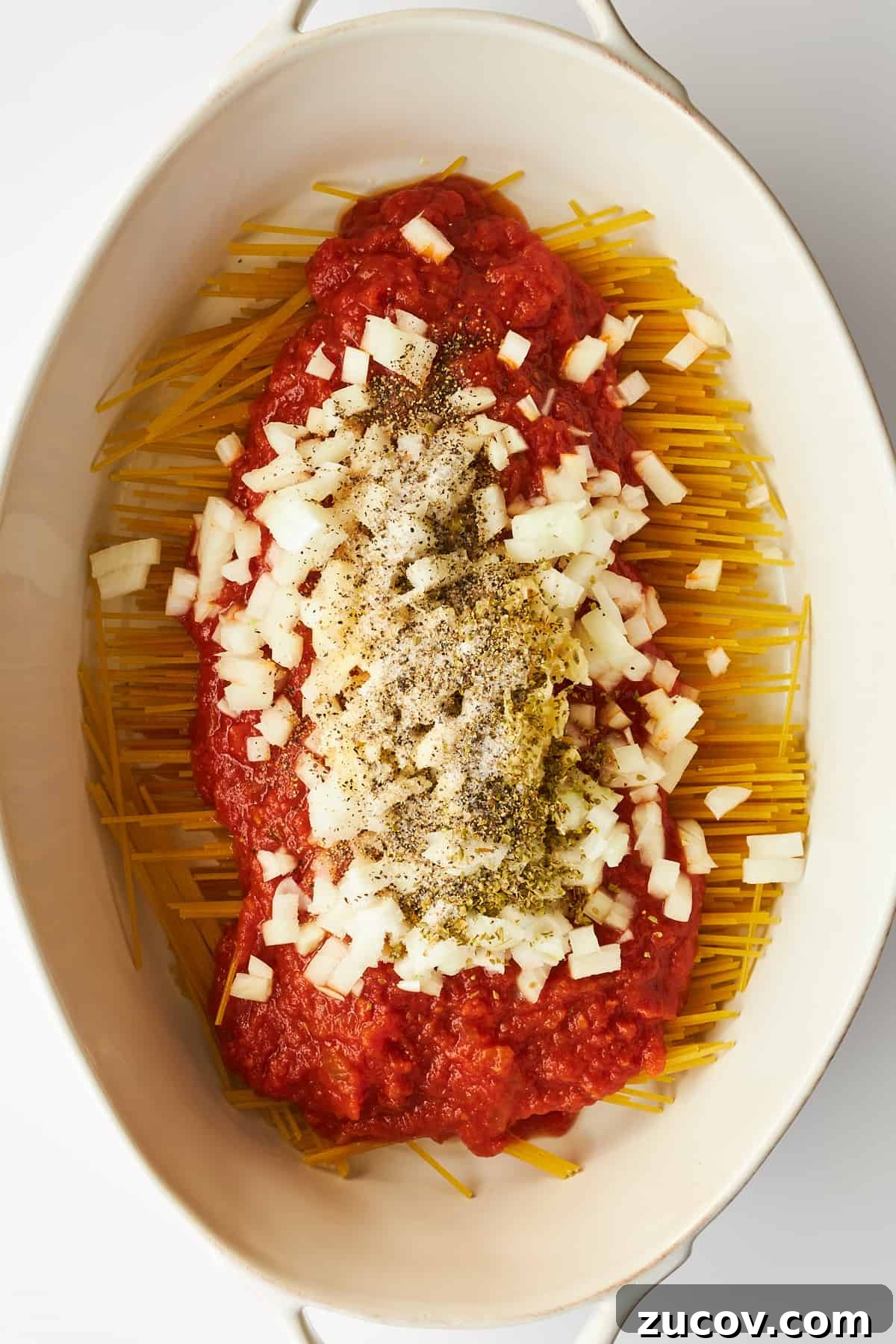 Cheesy Oven-Baked Spaghetti Casserole Recipe 6 Onions and seasonings on top of marinara sauce covering spaghetti noodles in an oval baking dish.