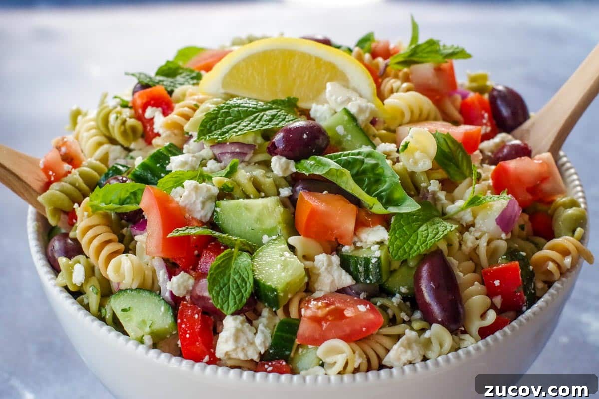 Greek Pasta Salad for Potlucks: Fresh Mediterranean Recipe 2 Close up photo of Greek pasta salad in a white bowl with a wooden fork and spoon (salad server).