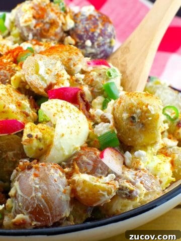Pierogi Potato salad in a Ukrainian print dish with wooden spoon and checkered red and white towel in the background