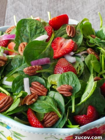 strawberry spinach pecan salad in a large bowl with flower print and wooden utensils