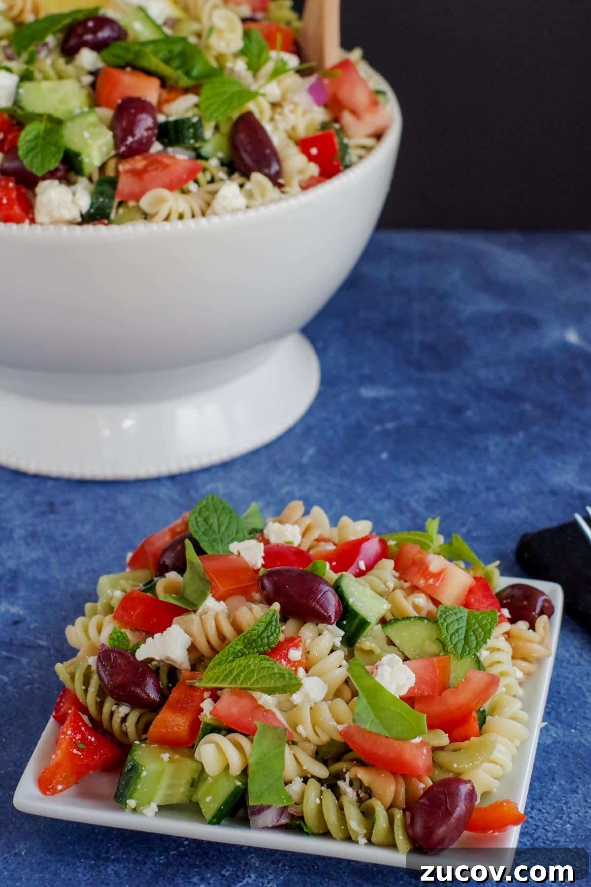 Greek Pasta Salad for Potlucks: Fresh Mediterranean Recipe 5 Greek pasta salad on a white plate with a white bowl of more pasta salad in the background.