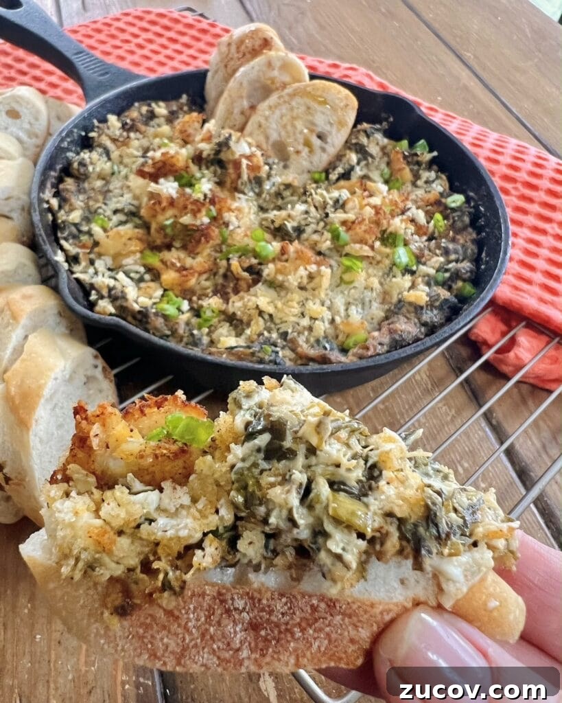 Creamy Baked Crab and Spinach Dip for Parties and Game Day 12 Close up of creamy spread on baguette slice with more dip in cast iron pan in background.