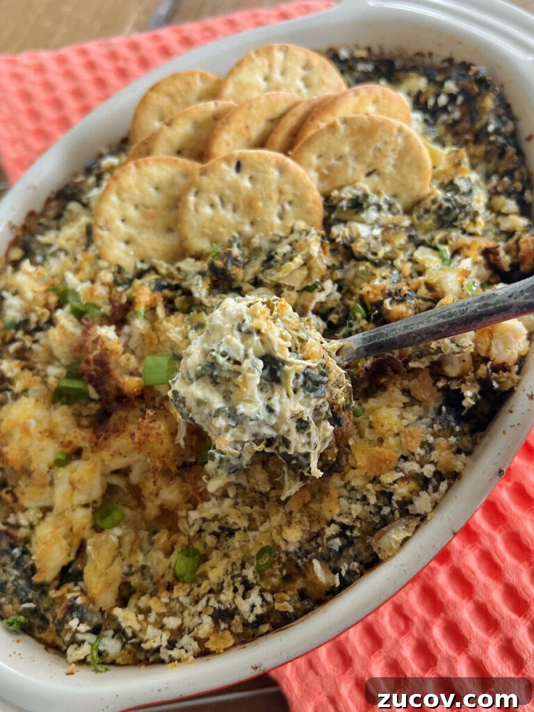 Creamy Baked Crab and Spinach Dip for Parties and Game Day 13 Close up of crab and spinach dip on spoon over casserole baking dish.