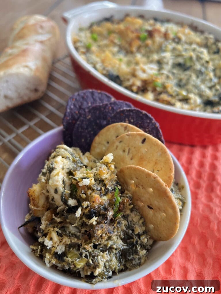Creamy Baked Crab and Spinach Dip for Parties and Game Day 3 Small dish with some spinach and crab dip, crackers and blue tortilla chips with full casserole dish of dip in background.