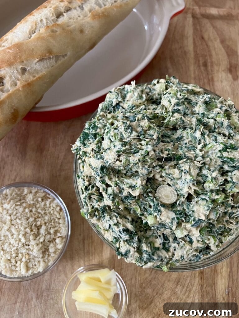 Creamy Baked Crab and Spinach Dip for Parties and Game Day 6 Stirred dip mixture, panko breadcrumbs and patts of butter in glass bowls on cutting boarl next to baguette.