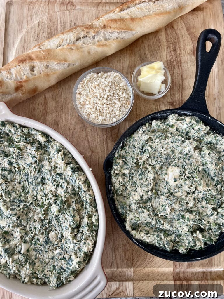 Creamy Baked Crab and Spinach Dip for Parties and Game Day 8 Dip mixture in two different baking dishes next to a baguette and two small bowls with breadcrumbs and pats of butter.