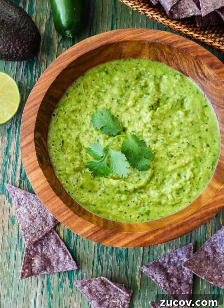 A wood bowl with green avocado salsa taco sauce and blue corn tortilla chips on the table.