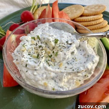 Creamy Herb and Garlic Dip Recipe for Parties and Snacks 14 Garlic and herb dip in a dish on a plate with chopped vegetables and crackers.