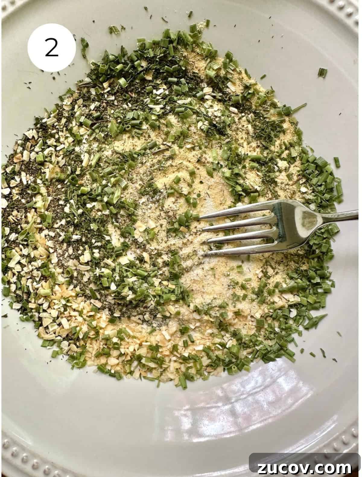 Creamy Herb and Garlic Dip Recipe for Parties and Snacks 5 A fork blending dried herbs and salt on a plate.