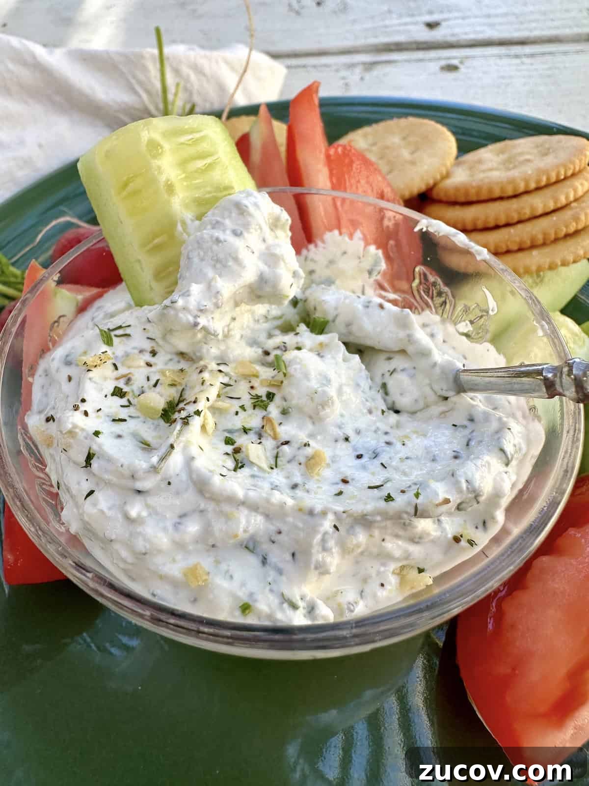Creamy Herb and Garlic Dip Recipe for Parties and Snacks 9 A slice of cucumber in a small bowl of herb and garlic dip on a plate.