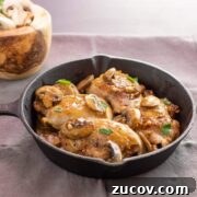 A cast iron pan with chicken mushroom and garlic in a sauce.