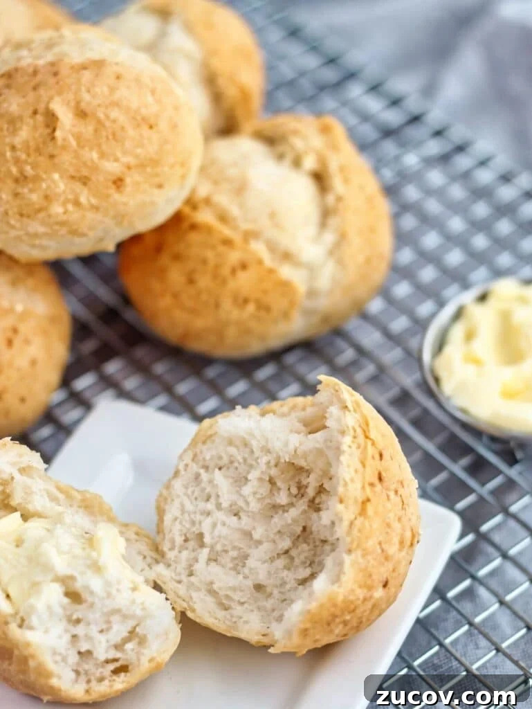 Crispy Gluten-Free French Rolls Recipe for Artisan Sandwiches 2 gluten free crusty french rolls on cooling rack with one roll split open on a small white square plate and butter to the side.
