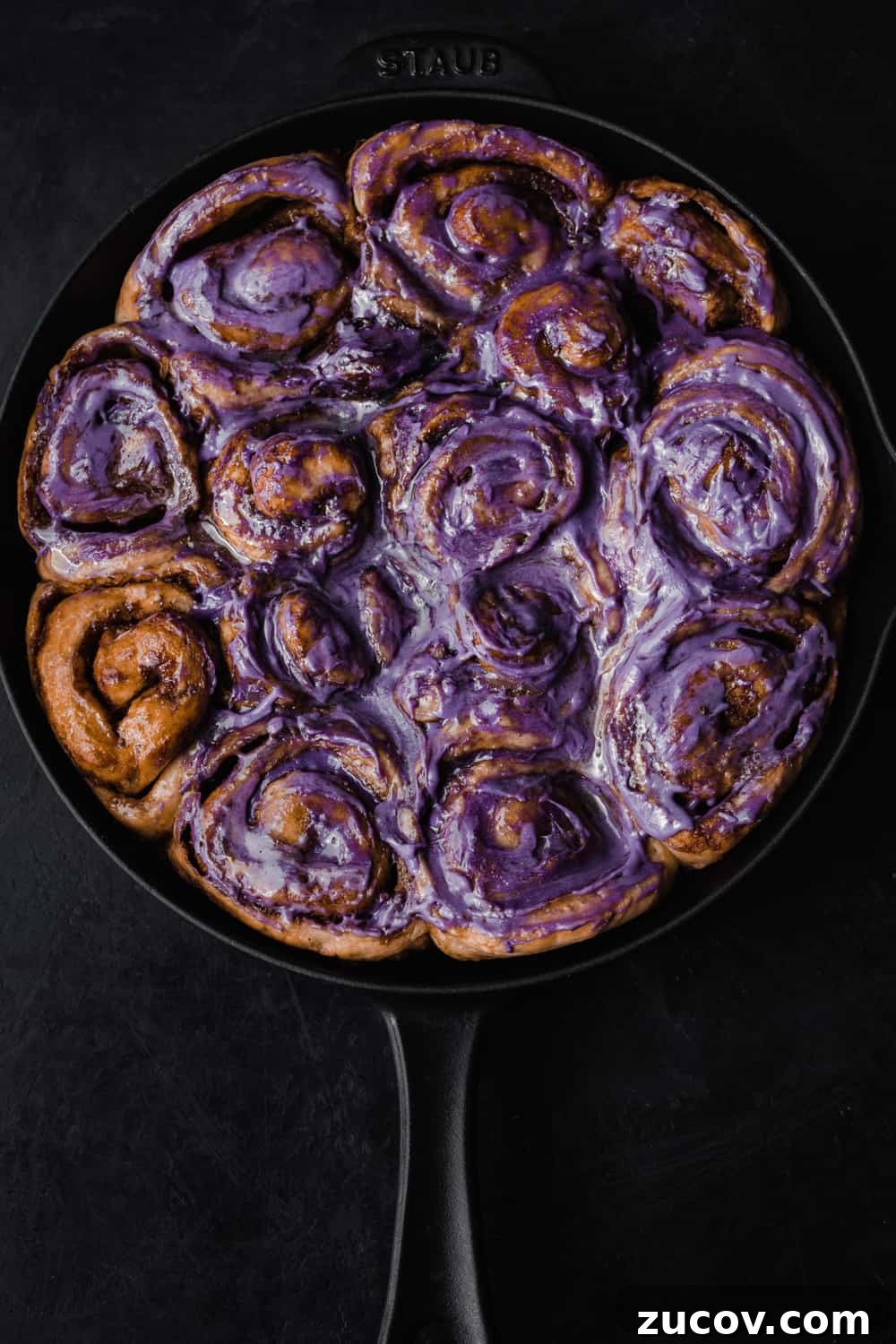 Cinnamon Rolls Made with Challah Dough: Soft, Buttery Recipe 6 Cinnamon rolls almost all frosted with a purple ube infused cream cheese icing; overhead shot on a black background.