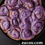 Challah Dough cinnamon rolls with an ube cream cheese frosting all done and ready to be eaten! Overhead shot on a black background.