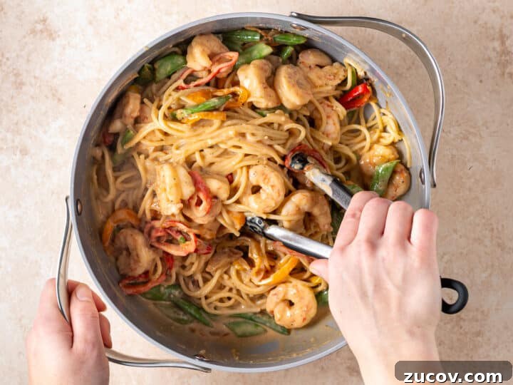 Tossing shrimp peanut noodles with snap peas and mini peppers in creamy peanut sauce