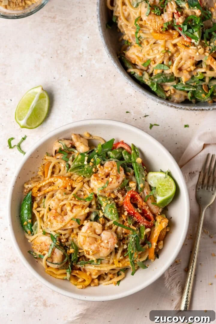 Plated peanut noodles with shrimp topped with Thai basil, green onions, and crushed peanuts
