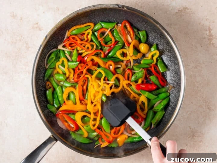 Snap peas, mini peppers, and shallots sautéing in black skillet