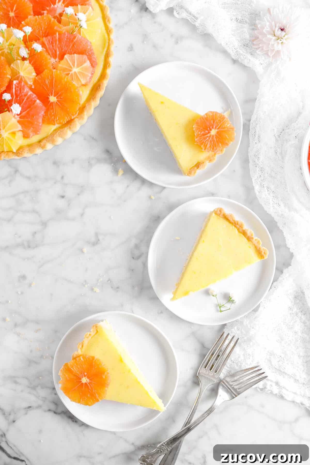 three slices of citrus tart on white plates with two forks and napkin