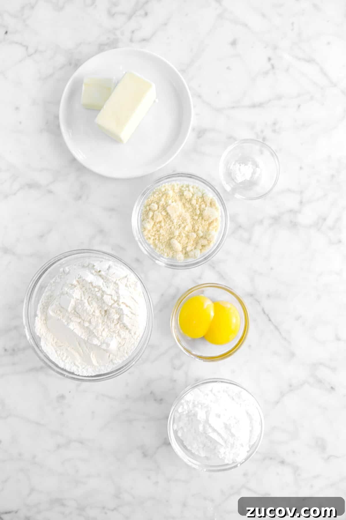 butter, almond flour, baking soda, eggs, flour, and powdered sugar on marble counter