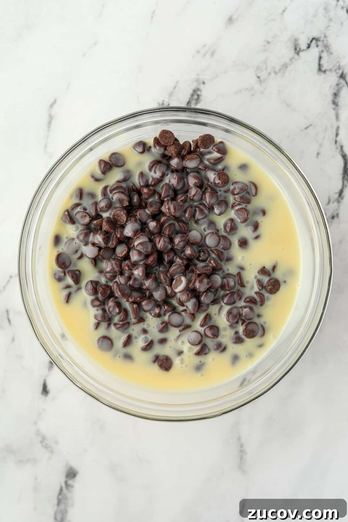 Decadent Chocolate Orange Truffles Recipe for Homemade Gifts 5 A large glass bowl filled with chocolate chips and sweetened condensed milk.