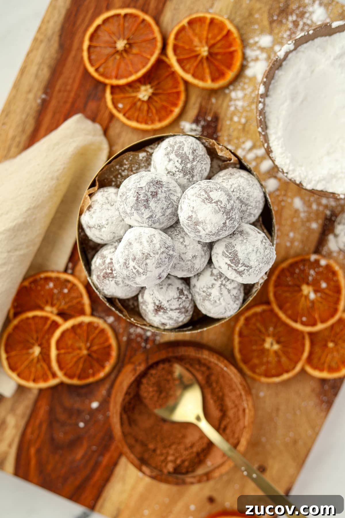 Decadent Chocolate Orange Truffles Recipe for Homemade Gifts 7 A bowl of truffles coated in powdered sugar, surrounded by dried orange slices.