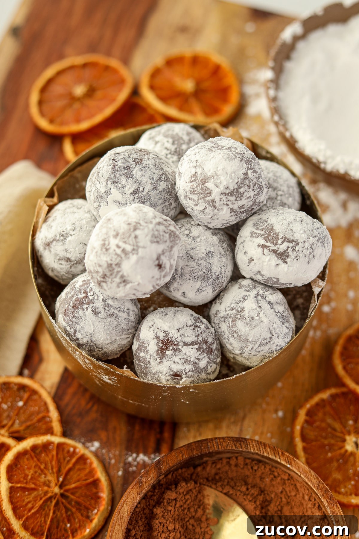 Decadent Chocolate Orange Truffles Recipe for Homemade Gifts 8 Chocolate balls coated in powdered sugar, with dried orange slices on the counter below.