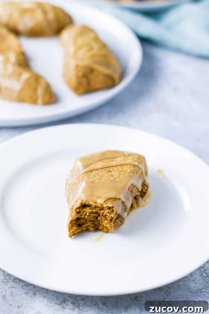 Pumpkin Glazed Scones with Maple Spice Frosting 9 A white plate with a scone with a bite taken out of it and a plate of scones in the background