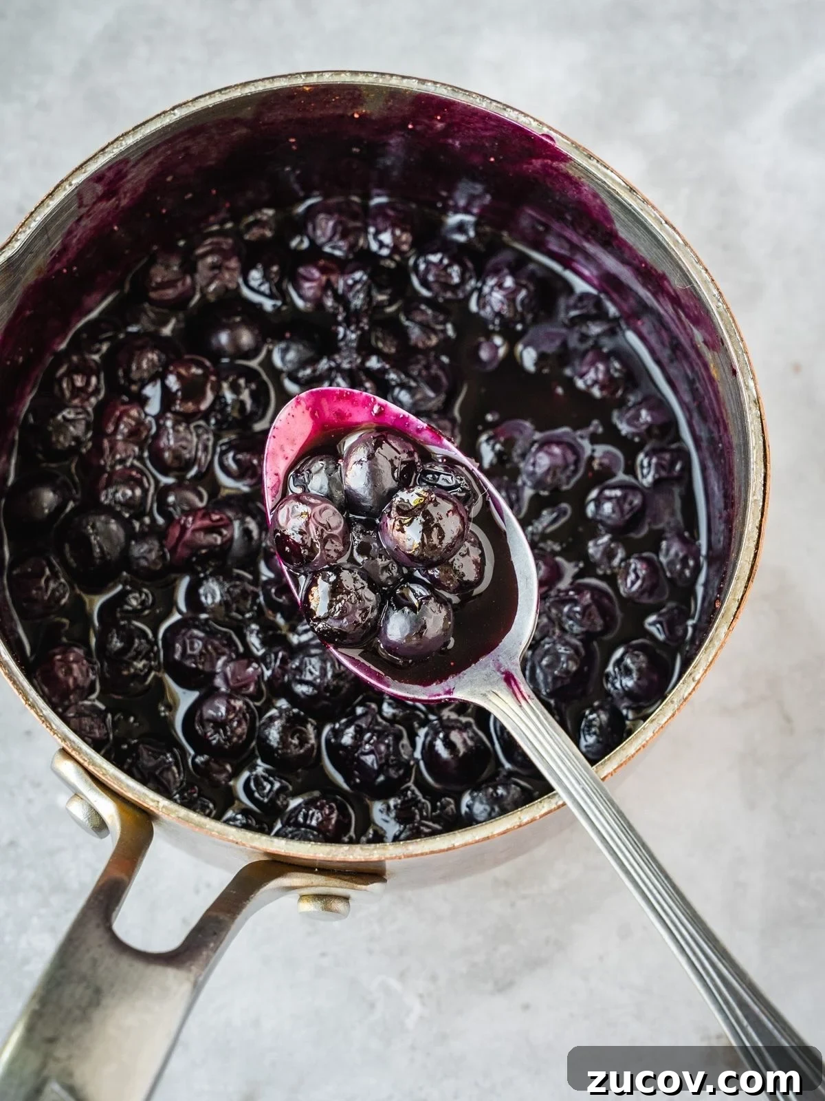 Maple Blueberry Compote Recipe for Pancakes and Yogurt 6 Blueberry Maple Compote in a saucepan with a spoon.