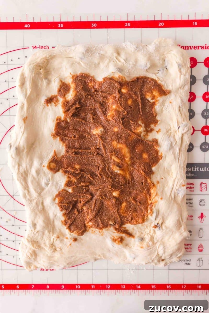 Sourdough Cinnamon Raisin Bread Recipe — Soft, Sweet & Spiced 11 Brown cinnamon butter mixture spread onto stretched rectangle of bread dough on floured surface. Hostess At Heart