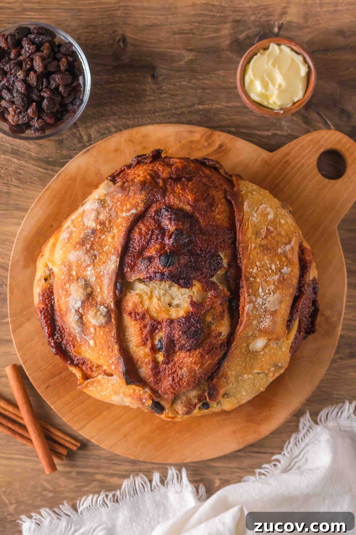 Sourdough Cinnamon Raisin Bread Recipe — Soft, Sweet & Spiced 15 Golden brown sourdough cinnamon raisin bread with visible raisins sitting on a cutting board. Hostess At Heart