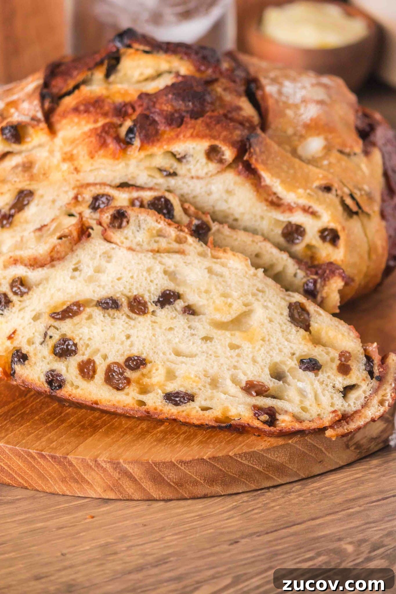 Sourdough Cinnamon Raisin Bread Recipe — Soft, Sweet & Spiced 16 Front view of a loaf of raisin cinnamon sourdough bread sitting on a cutting board with the first two slices cut showing plump raisins and cinnamon swirls throughout a tender crumb. Hostess At Heart