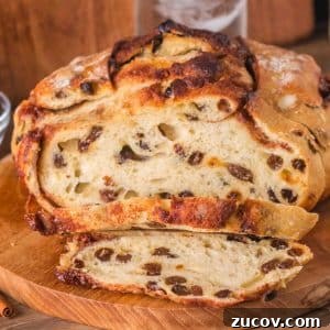 Sourdough Cinnamon Raisin Bread Recipe — Soft, Sweet & Spiced 18 Front view of a loaf of overnight sourdough cinnamon raisin bread sitting on a cutting board with the first two slices cut showing plump raisins and cinnamon swirls throughout a tender crumb. Hostess At Heart